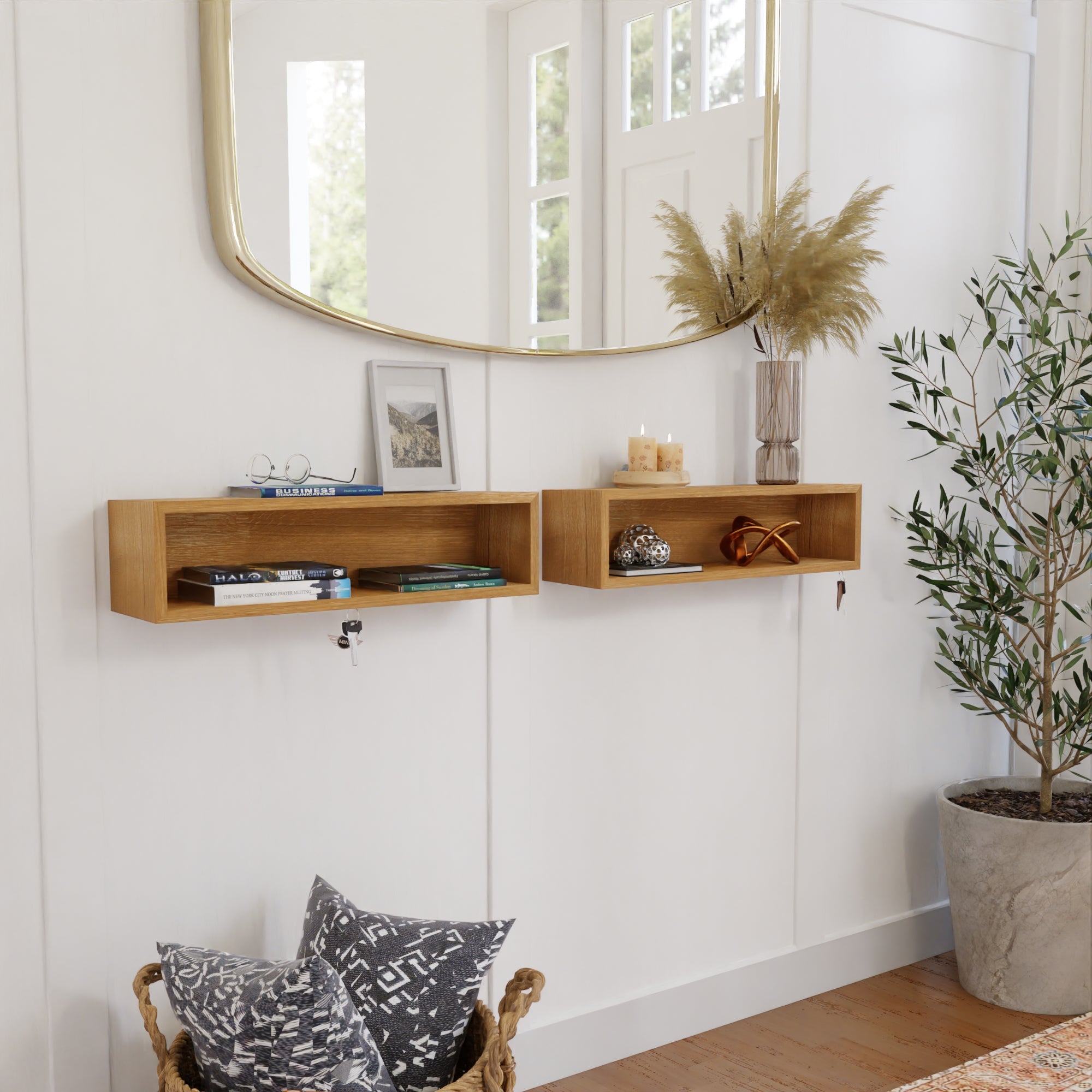 A stylish entryway with a large mirror, two wooden wall shelves, books, decorative items, a vase with dried grasses, a plant, and a basket with patterned cushions on the floor. Natural light filters in.