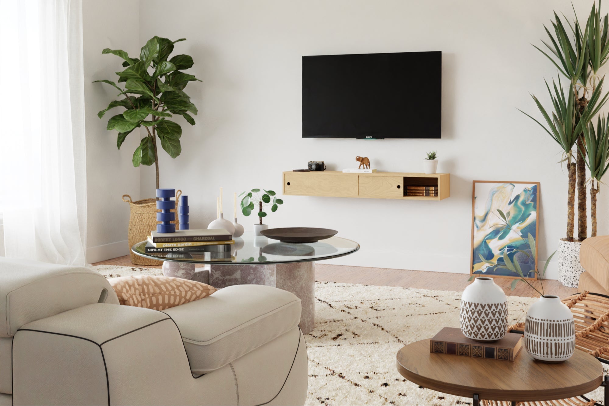 A modern living room with a wall-mounted TV, beige sofa, circular glass coffee table, potted plants, and minimalistic decor. A light patterned rug covers the wooden floor, and a painting leans against the wall.