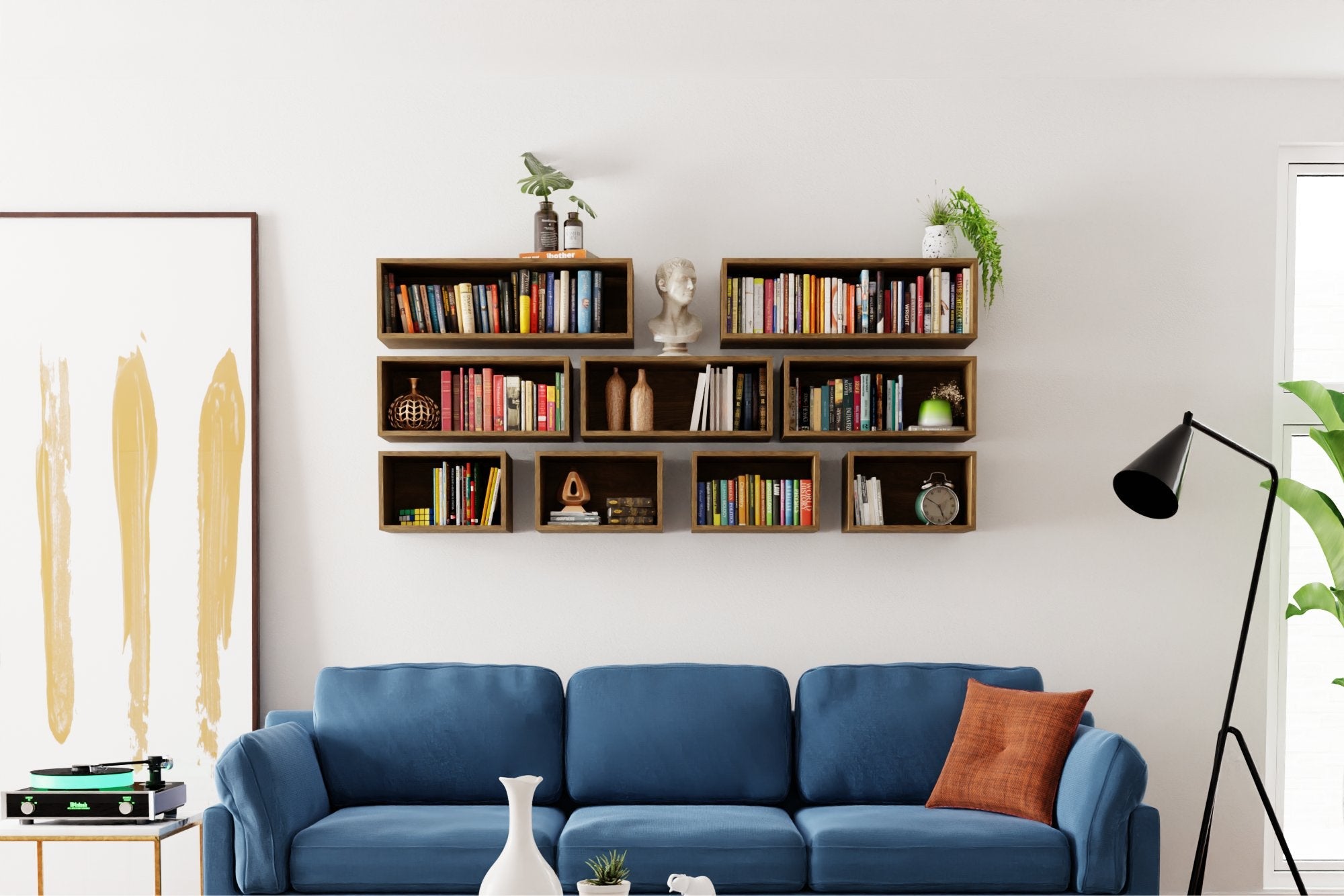 A modern living room with a blue sofa, an orange cushion, and a floor lamp. Above, a floating wooden bookshelf displays various books and decor items. A large abstract painting and potted plants add style to the space.