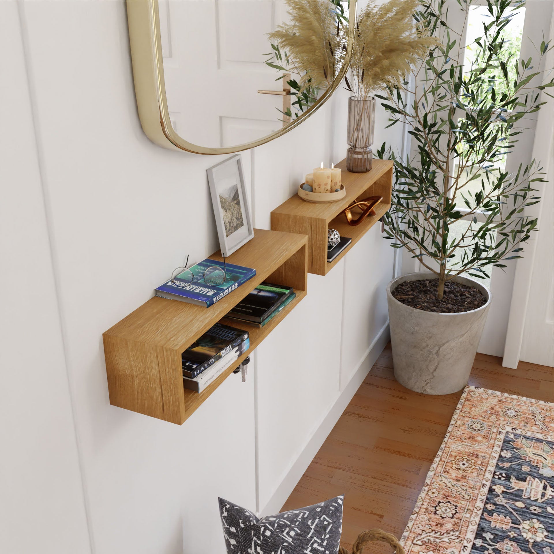 A stylish hallway features wooden floating shelves by Krovel Furniture Co., holding books, candles, and decor. A large mirror hangs above, with pampas grass in a vase nearby and an ornate carpet on the floor. These handmade elements add a cozy and modern touch to the space.