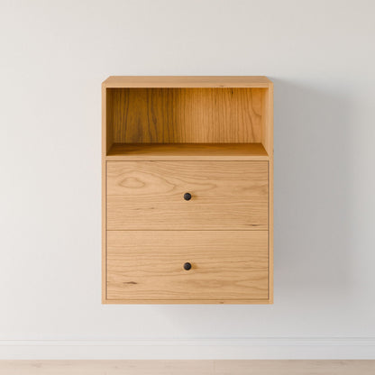 A wall-mounted Krovel Furniture Co. "Closet Drawers and Shelves in Cherry" features solid Maple drawers with small black knobs, a modular shelf system on top, a natural finish against a plain white wall, and rests above a light wood floor. 