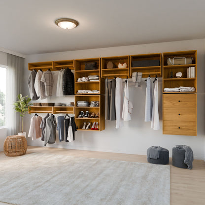 A modern walk-in closet showcases Krovel Furniture Co.'s Closet Drawers and Shelves in Cherry, part of a sleek modular system. Clothes, shoes, and accessories are neatly arranged. Two round cushions rest on the floor, and a wicker basket with a plant adds to the neutral palette by the window. 