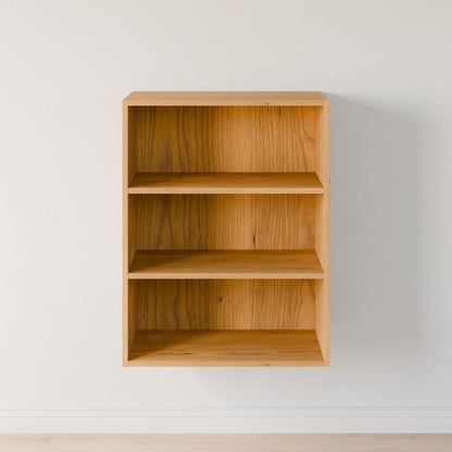 The Closet Drawers and Shelves in Cherry by Krovel Furniture Co., a compact wooden wall-mounted bookshelf with three shelves, stands against a white wall. Its minimalist, modular-like design casts a subtle shadow on the matching floor, with empty shelves ready for personalized décor. 