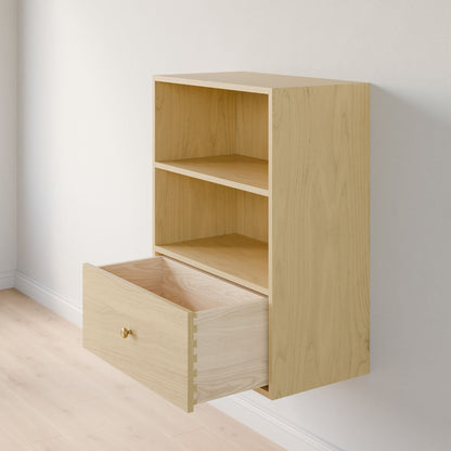 The Closet Drawers and Shelves in Maple by Krovel Furniture Co. is a wooden wall-mounted shelf made from premium plywood, featuring two open compartments, a large dovetail drawer with a gold knob, elegantly mounted against a white wall on a light wood floor. 