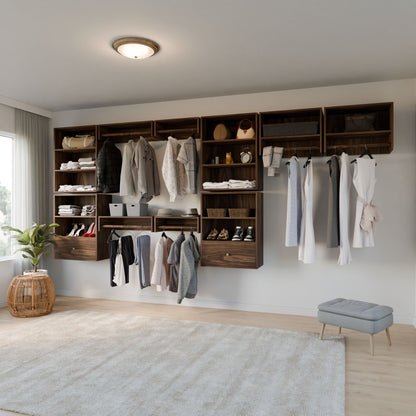 The Krovel Furniture Co. Closet Drawers and Shelves in Walnut neatly organize clothing, bags, and boxes with wooden shelves and dovetail hangers. A small gray stool and a plant in a woven basket sit on the light wood floor near a large window. 