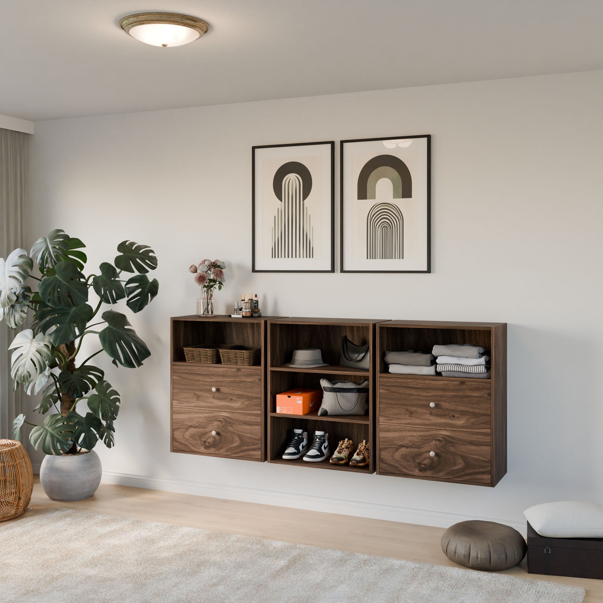 A modern living room includes a beige carpet, a large potted plant, and three Krovel Furniture Co. Closet Drawers and Shelves in Walnut with a modular design, storing shoes, folded clothes, and decor. Two abstract framed artworks hang above while a round ceiling light softly illuminates the space. 