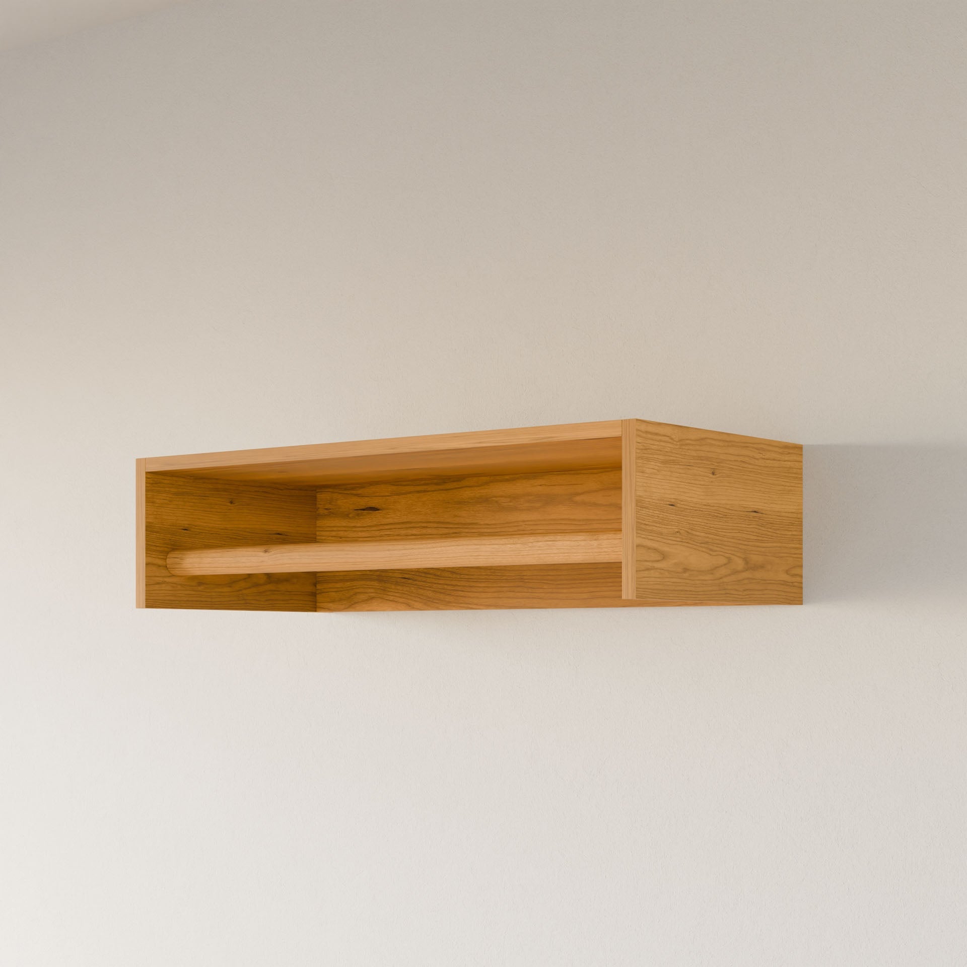 The Closet Hanger in Cherry by Krovel Furniture Co. is a wooden wall-mounted shelf, handcrafted in Portland, Maine from premium grade plywood. Its simple rectangular design features a natural wood grain finish and an open front, perfect for storage or display against a plain white wall.