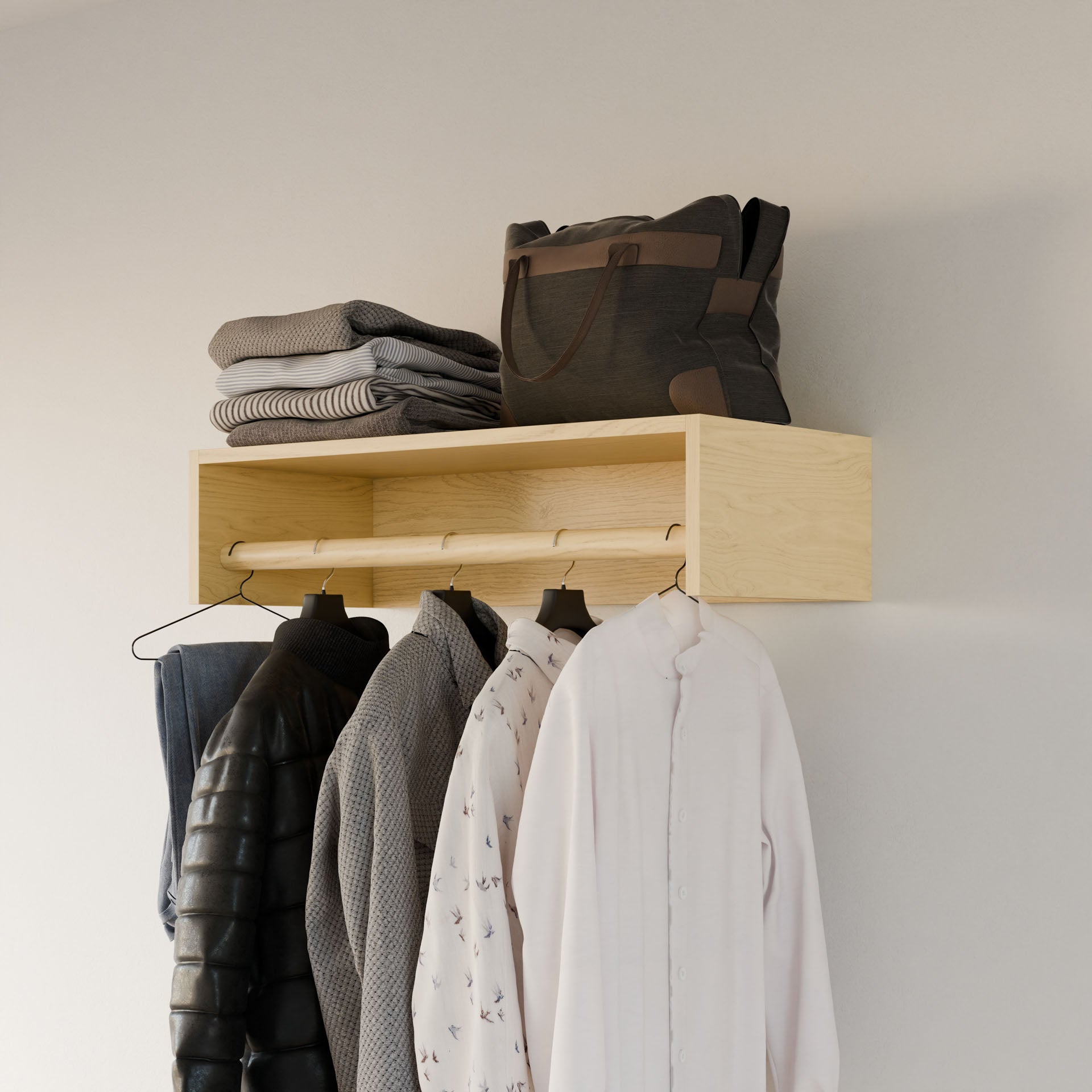 Krovel Furniture Co.'s Closet Hanger in Maple complements the wooden wall-mounted shelf displaying folded gray sweaters and a black bag. Below, a clothing rack with premium-grade plywood supports garments like black and white jackets on sleek hangers against a plain light-colored wall.