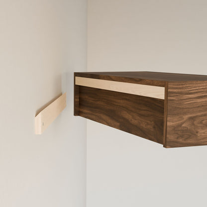 The Krovel Furniture Co. Closet Hanger in Walnut, crafted from premium grade plywood with a two-tone dark wood and lighter front strip, is being mounted on a wall. A bracket aligns perfectly with the cabinet edge for secure installation.