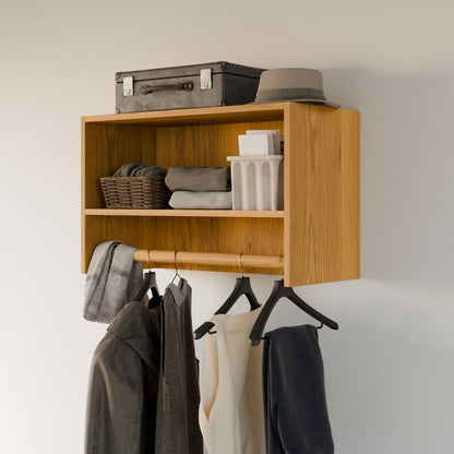 The Closet Hanger with Shelf in Cherry by Krovel Furniture Co. features open compartments for a gray suitcase, hat, basket, folded clothes, and containers. A wooden rod underneath supports modular hangers holding jackets and a white shirt against a plain wall.