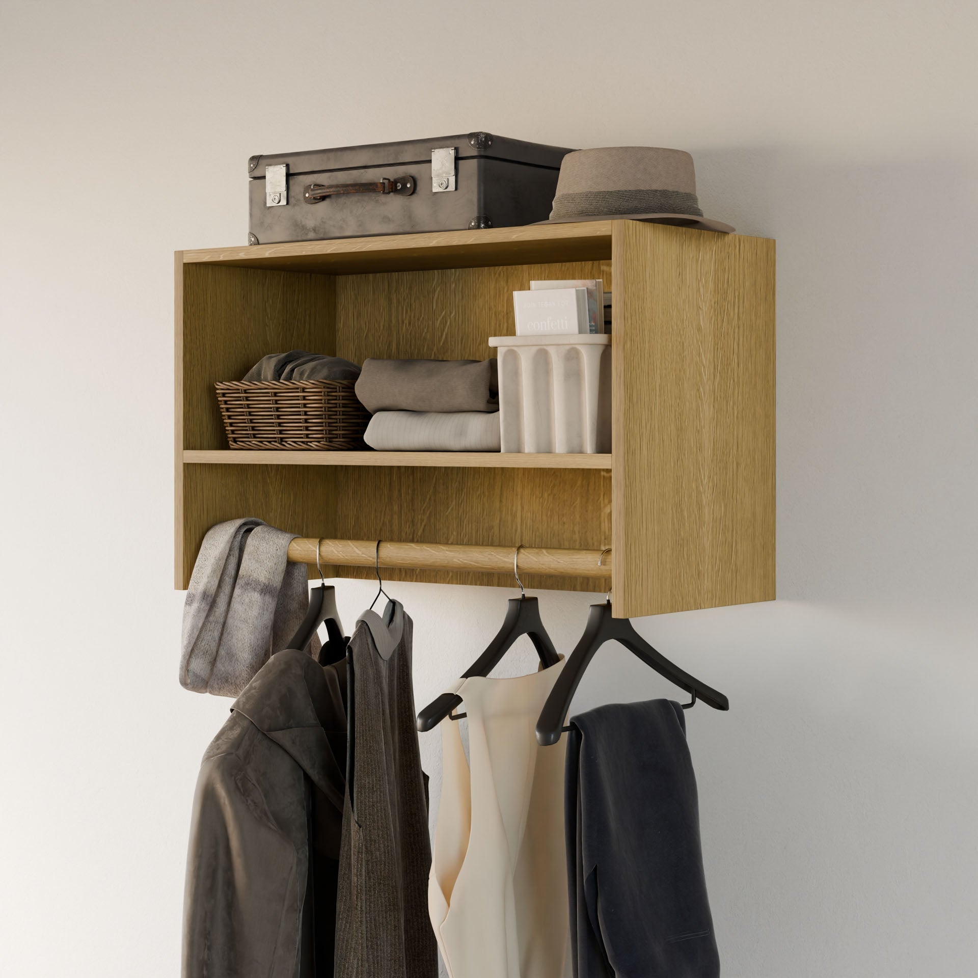 The Closet Hanger with Shelf in White Oak by Krovel Furniture Co. features two premium plywood compartments. The top holds a suitcase, hat, and basket; the middle accommodates folded clothes and a container. Below is a modular closet hanger supporting three hangers with draped clothing.