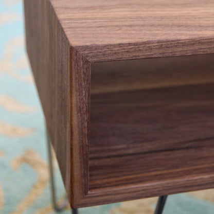 Close-up of the Krovel Coffee Table in Walnut, showcasing its mid-century modern design with a smooth, rectangular shape. Crafted from rich black walnut, it is supported by stainless steel hairpin legs and sits atop a blue and beige patterned rug.