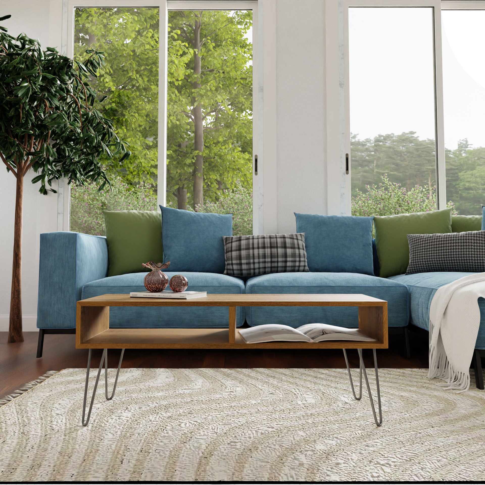 A modern living room showcases a large blue sectional sofa adorned with green and plaid cushions. In the center, a Krovel Coffee Table in White Oak stands elegantly on a circular woven rug. Expansive windows frame views of lush green trees outside, while a potted plant adorns the corner, enhancing the mid-century modern allure.