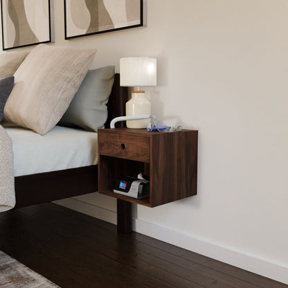 A minimalist bedroom exudes a Mid-Century Modern ambiance with a Krovel CPAP Nightstand in Walnut, crafted with precision and featuring both a drawer and an open shelf. A small lamp and medical device occupy the nightstand, while the bed is adorned with a light duvet over its dark wooden frame.