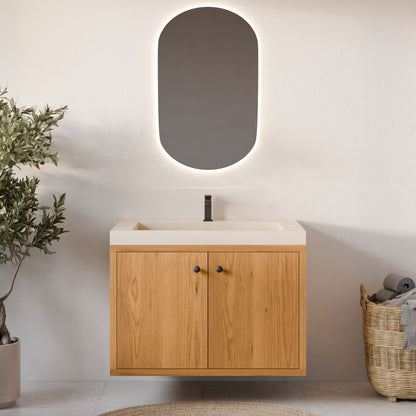 A modern bathroom showcases the Krovel Furniture Co.'s floating Double Door Vanity in Cherry with soft-close hinges, paired with a rectangular sink and sleek black faucet. An oval mirror above has subtle backlighting. To the left is a potted plant; to the right, a woven basket holds rolled towels.