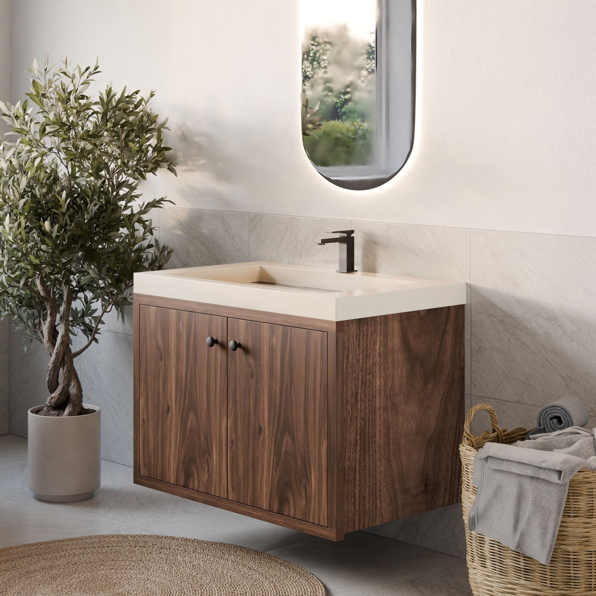 A modern bathroom features Krovel Furniture Co.'s Double Door Vanity in Walnut with a rectangular sink. A round mirror hangs above, an olive tree sits on the left, and soft-close hinges add sophistication. A woven towel basket adorns the floor, while natural light brightens the room.