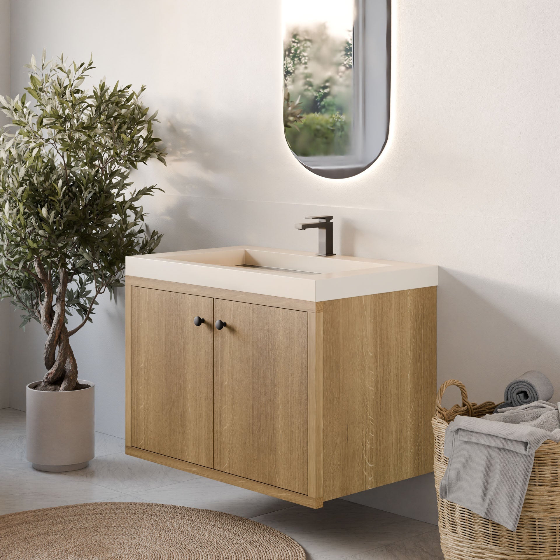 In a serene bathroom, Krovel Furniture Co.'s Double Door Vanity in White Oak features a hardwood veneer, rectangular sink, and modern faucet. An LED-lit oval mirror hangs above, with a potted plant on the left and a wicker basket of towels on the right against the white wall.