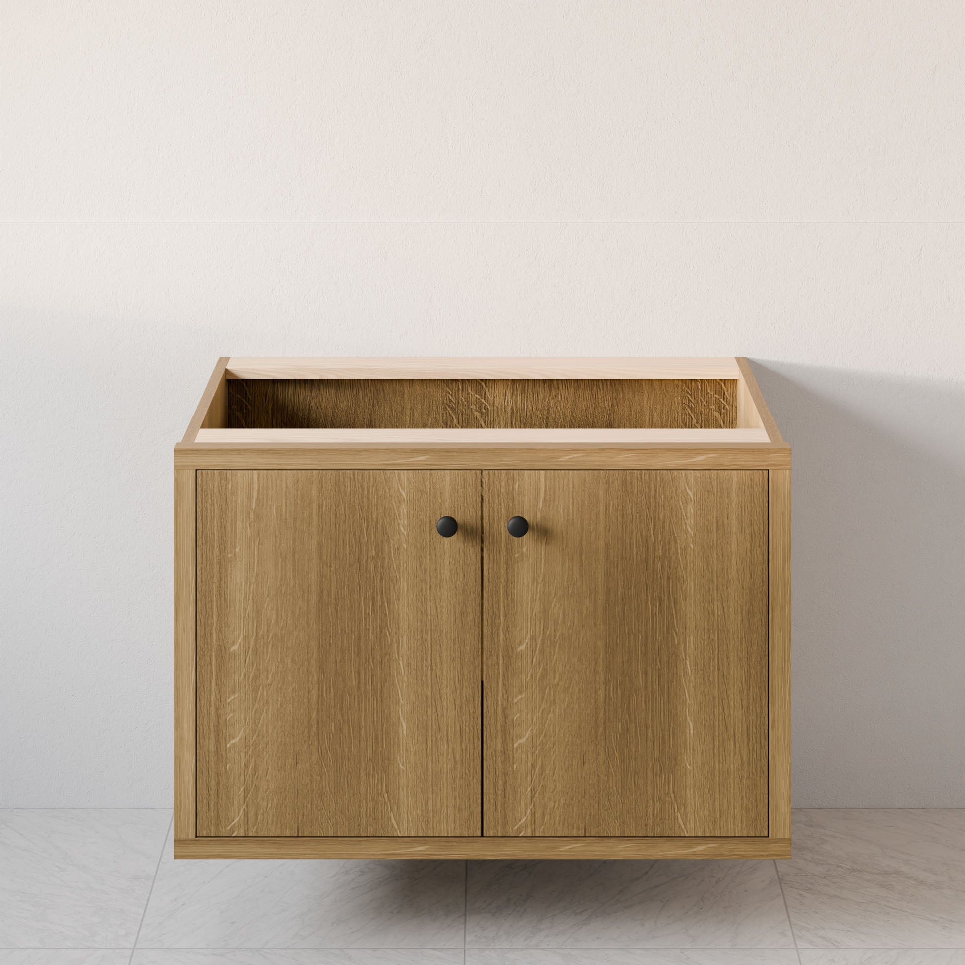 The Double Door Vanity in White Oak by Krovel Furniture Co. is a floating wooden bathroom cabinet with black knobs against a light wall and tiled floor. Its hardwood veneer top is unfinished for easy sink installation, and it includes soft-close hinges for convenience.