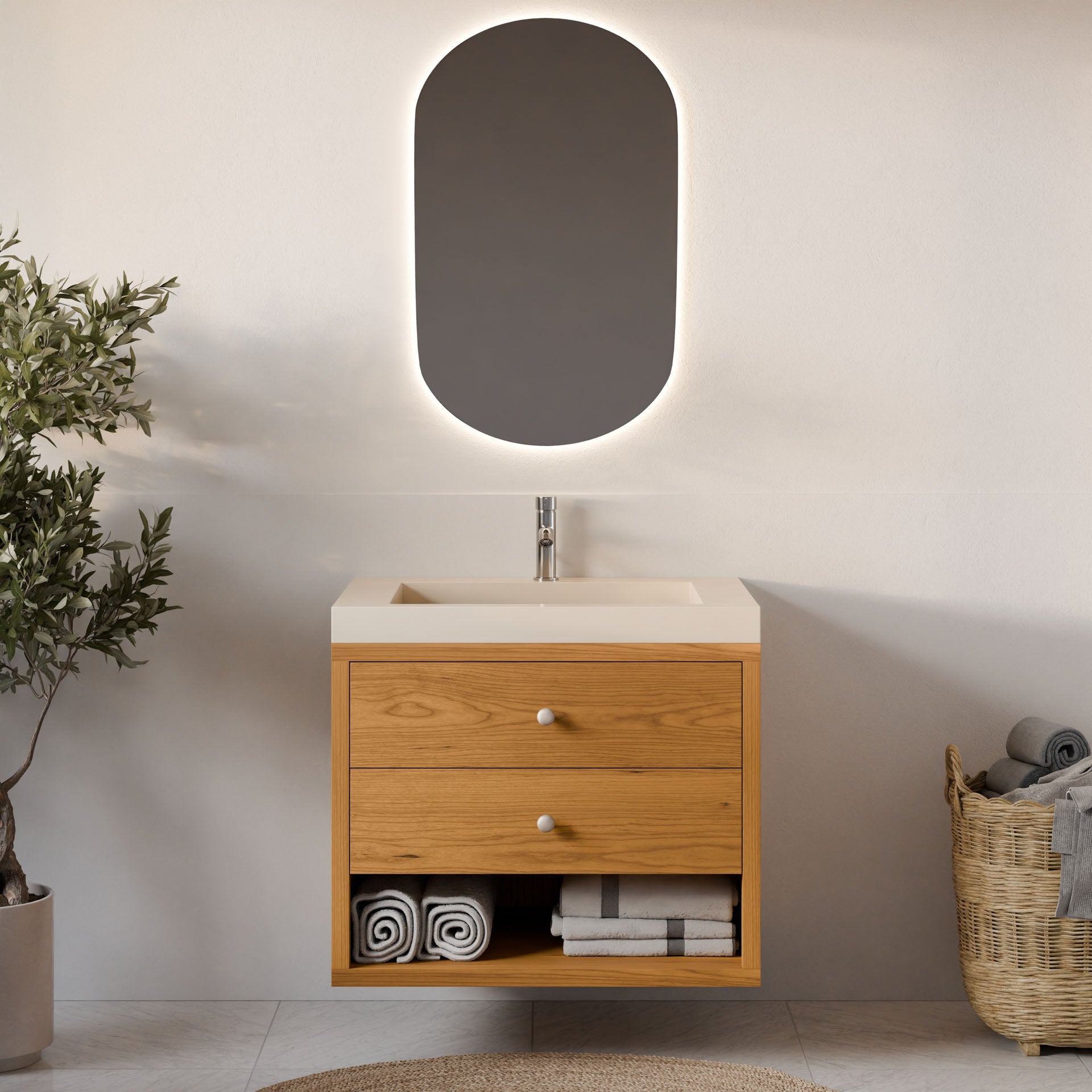 A minimalist bathroom features Krovel Furniture Co.’s Double Drawer, Open Shelf Vanity in Cherry with dovetail joinery, integrated sink, and drawers. An oval backlit mirror hangs above, complemented by a woven basket holding rolled towels.