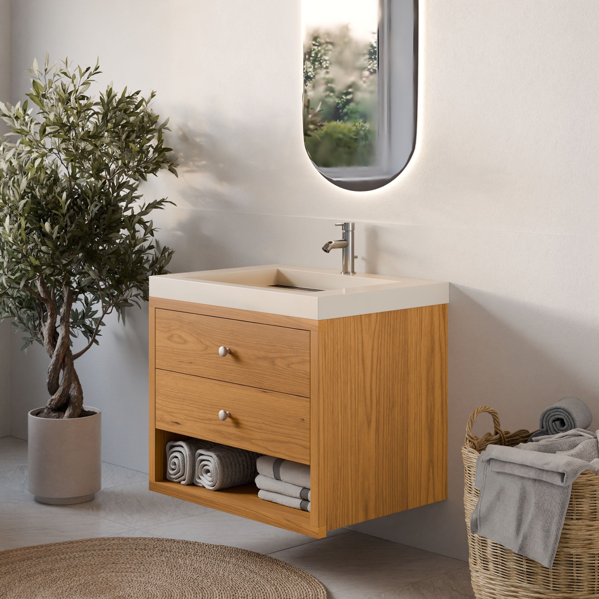 A modern bathroom showcases Krovel Furniture Co.'s Double Drawer, Open Shelf Vanity in Cherry with a square sink and faucet. Rolled towels are neatly arranged below, a basket with folded towels sits beside an olive tree, and an oval mirror hangs above.