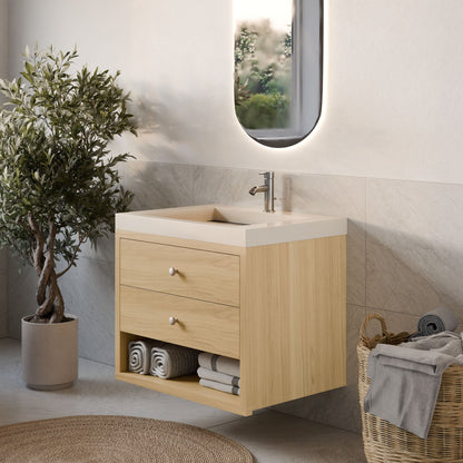 A modern bathroom features Krovel Furniture Co.'s Double Drawer, Open Shelf Vanity in Maple with a rectangular sink and oval mirror. Rolled towels rest on the hardwood veneer shelf, accompanied by a wicker basket and custom potted plant on a light-colored tile floor.