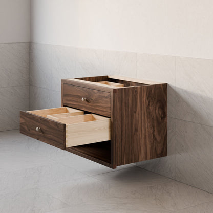 The Double Drawer Open Shelf Vanity in Walnut by Krovel Furniture Co. features hardwood veneer and dual open drawers with a natural wood grain finish. Custom-sized, it mounts to a light gray tile wall above a matching floor for a minimalist, modern look.