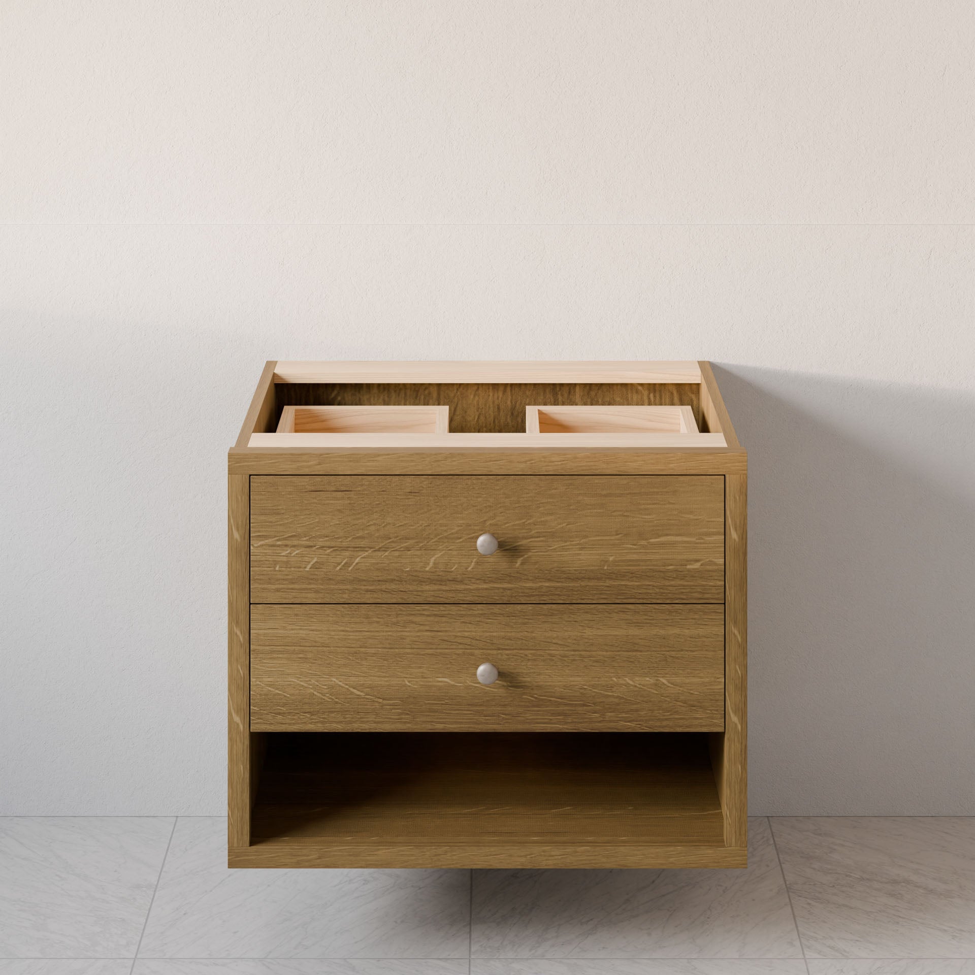 The Double Drawer, Open Shelf Vanity in White Oak by Krovel Furniture Co. features two drawers with round silver handles and a natural hardwood veneer. It has an open top without countertop or sinks and is designed for installation against a light-colored wall on a tiled floor.