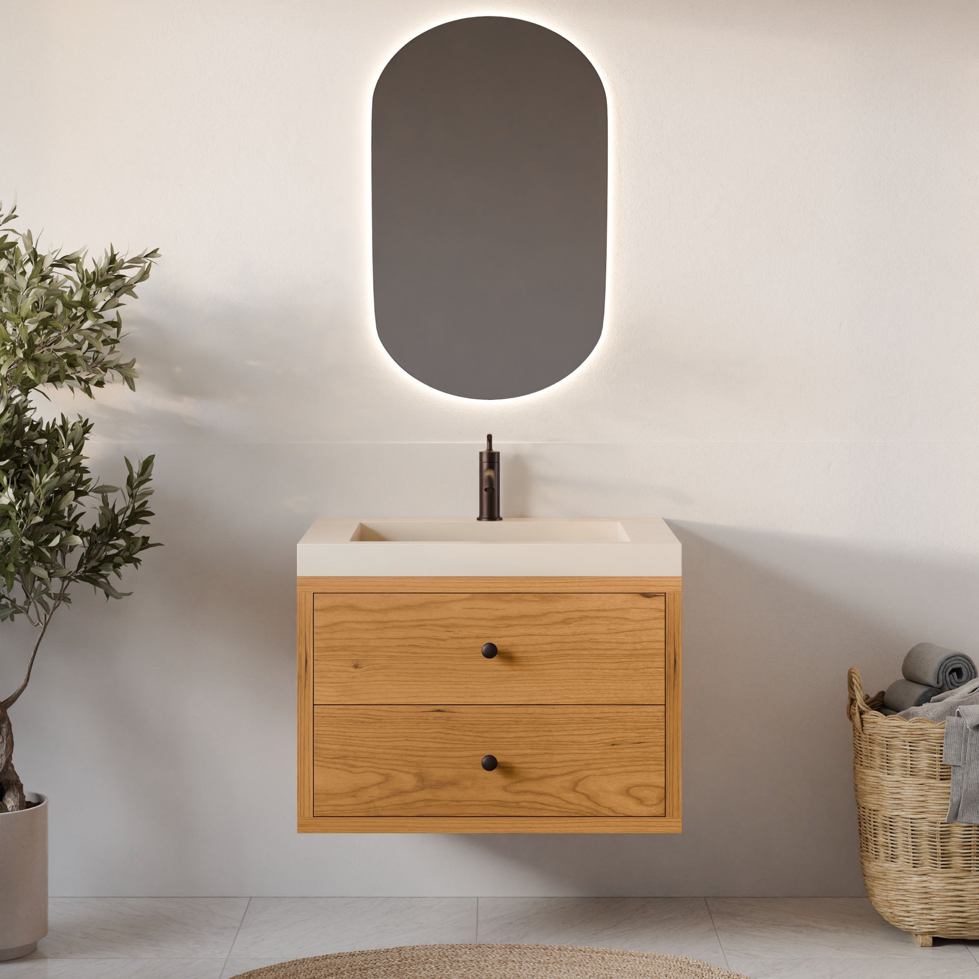 A minimalist bathroom showcases a custom-size Double Drawer Vanity in Cherry by Krovel Furniture Co. An oval mirror is positioned above a white sink featuring a centered black faucet, with a plant on the left and a towel basket on the right adding natural touches to the sleek design.