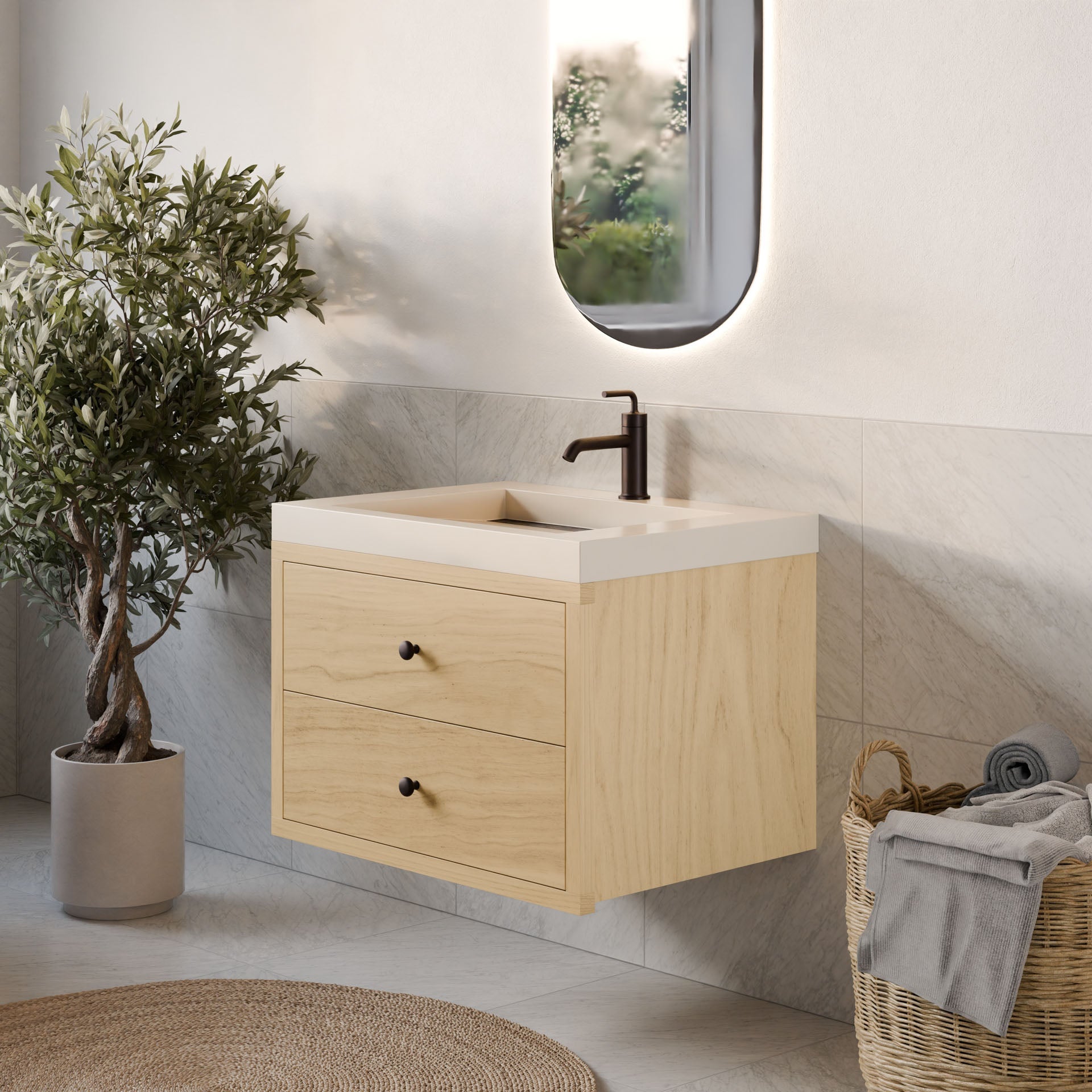 A stylish bathroom showcases the Krovel Furniture Co. Double Drawer Vanity in Maple with dovetail joinery, white countertop, and black faucet. An oval backlit mirror hangs above, while a wicker basket with towels and a potted olive tree enhance the natural charm of the gray-tiled floor.