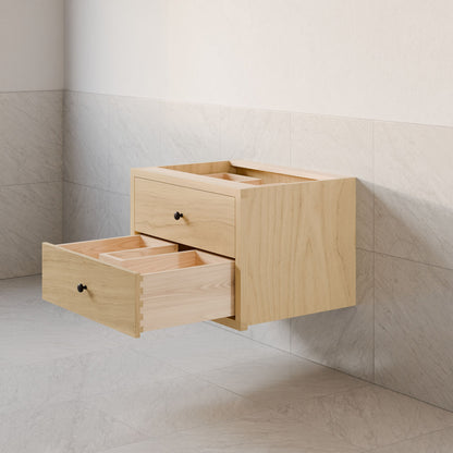 The Double Drawer Vanity in Maple by Krovel Furniture Co. is a minimalist floating wooden design with two open drawers featuring hardwood veneer and simple black knobs. It showcases light wood grain and dovetail joinery against a backdrop of light gray tiled walls and floors.