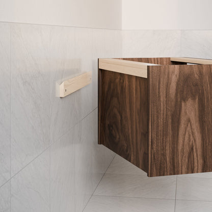 A partially open Double Drawer Vanity in Walnut by Krovel Furniture Co., featuring a customized design, is wall-mounted in the room's corner. Light gray marble tiles cover the surrounding wall and floor, with a horizontal wooden strip attached beside this floating vanity.