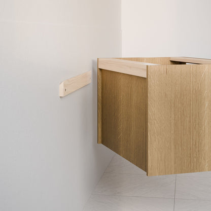 A partially installed Double Drawer Vanity in White Oak by Krovel Furniture Co. is mounted on a white wall with a wooden support bar, and the tiled floor features a white and gray pattern.