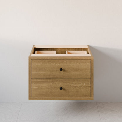 The Double Drawer Vanity in White Oak by Krovel Furniture Co. features soft-close drawers and simple black knobs. Mounted on a light-colored wall above a tiled floor, the open top section offers additional storage or decorative use, highlighting its elegant hardwood veneer finish.