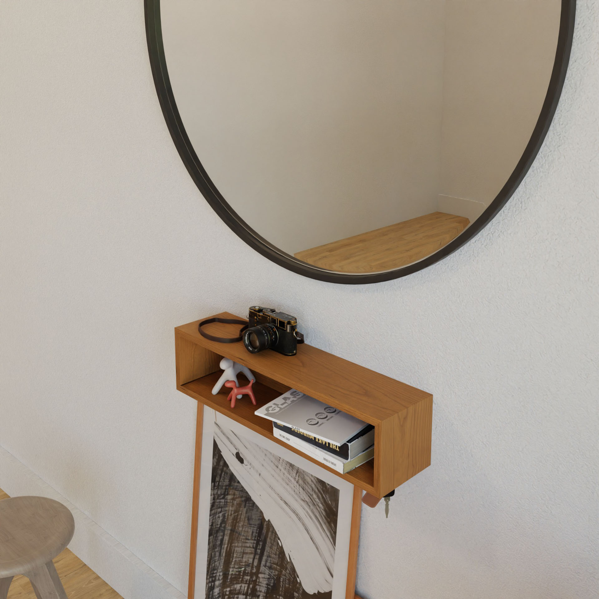 A minimalist room displays a round mirror above Krovel's Entryway Organizer in Cherry on a white wall, adorned with a vintage camera, books, sunglasses, and a small figurine. A framed black and white artwork leans below while a wooden stool stands nearby.