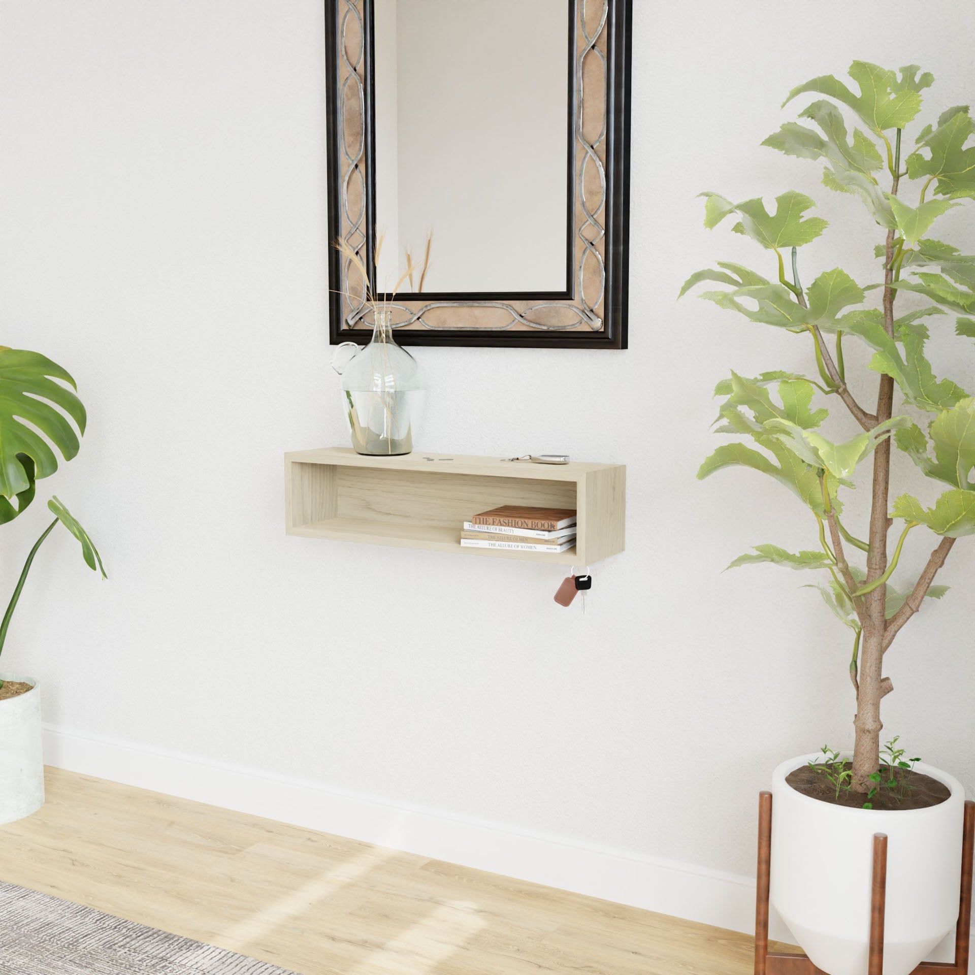 A minimalist room includes a Krovel Entryway Organizer in Maple with a clear vase holding one leaf and a small item. Above hangs a framed mirror. To the left, there's a large potted green plant; to the right, a smaller plant in a white pot rests on the floor.