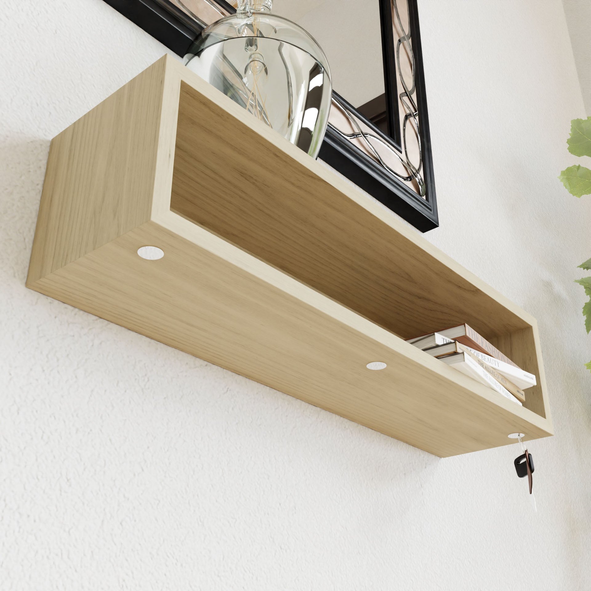 A minimalist Entryway Organizer in Maple by Krovel is mounted on a white wall using a french-cleat mount. It holds a transparent vase with a plant and a few small books, while a mirror with a black frame is partially visible above the shelf.