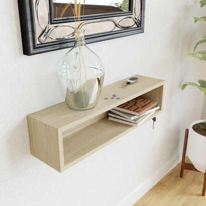 An entryway organizer crafted from maple by Krovel holds a large glass bottle with reeds, several coins, car keys, and a stack of books. Above the shelf hangs a decorative mirror secured by a French-cleat mount, with a potted plant partially visible to the right.