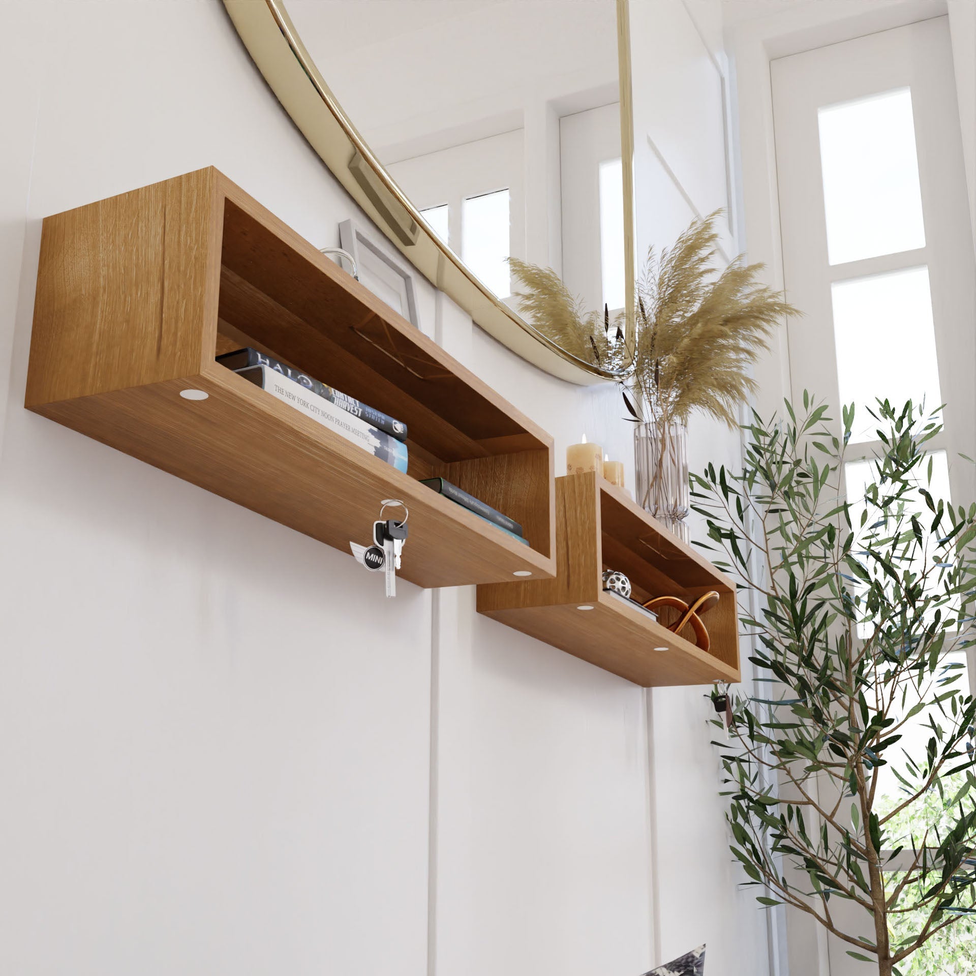 Krovel's Entryway Organizer in White Oak, wall-mounted beneath a large round mirror, displays books, a candle, and decor on shelves. Keys hang from one shelf like in a floating organizer. Pampas grass in a vase and a potted plant adorn the area near the window.