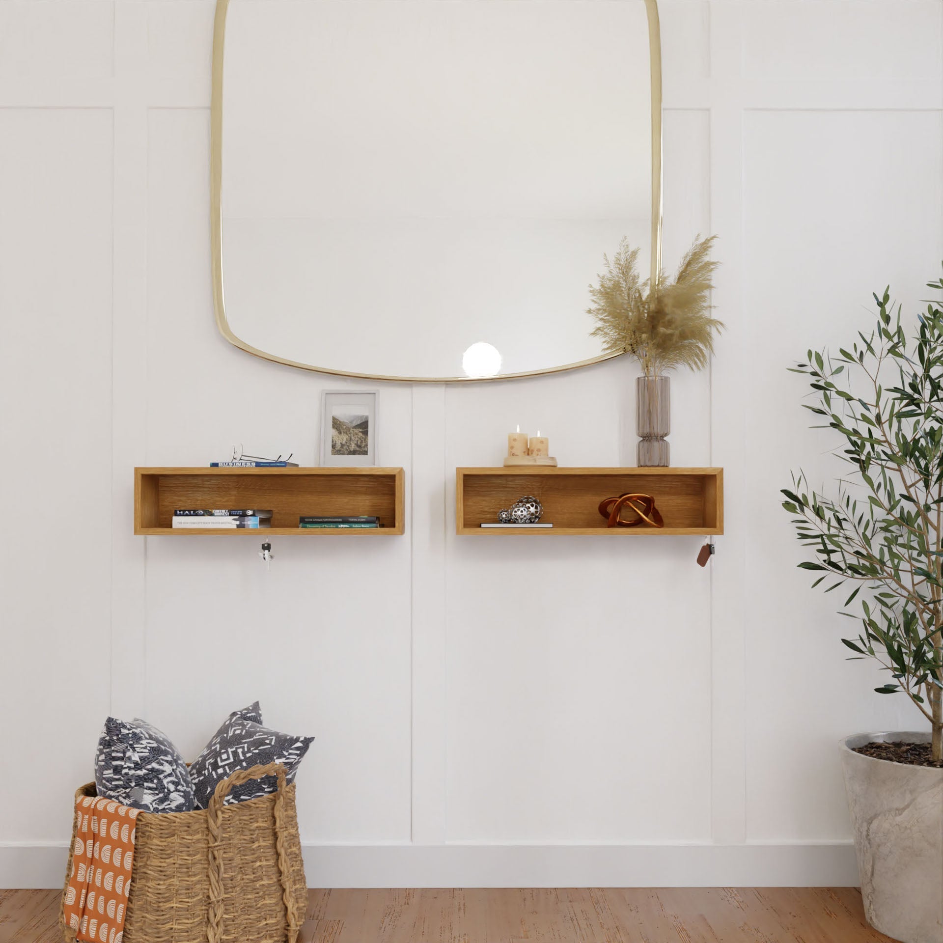 A minimalist room showcases a large, square mirror on a white paneled wall. Below it, two Krovel Entryway Organizers in White Oak display decor. A potted plant sits to the right, while patterned pillows fill a basket to the left on the wooden floor.