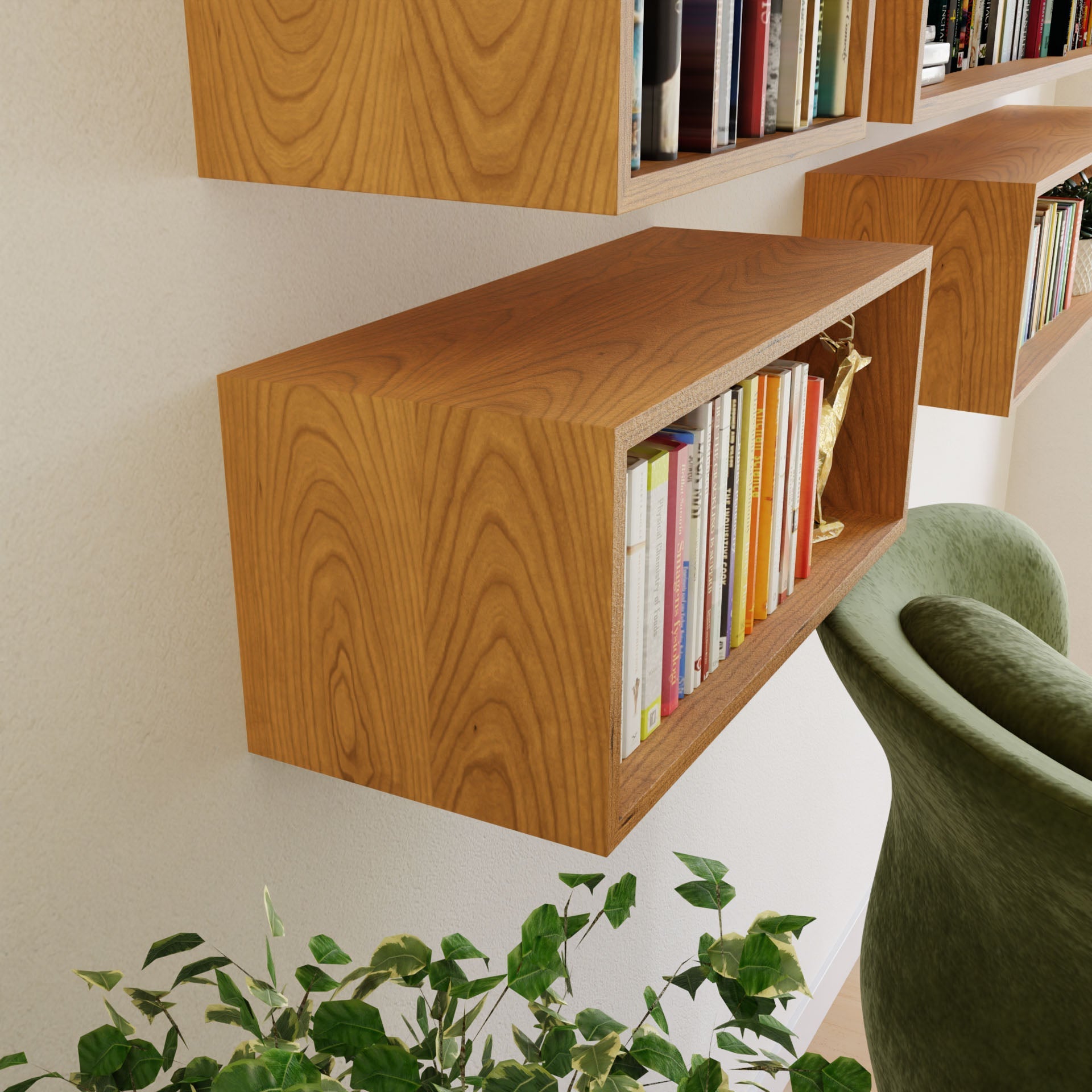 The Krovel Floating Bookshelf in Cherry, possibly mounted with a French cleat, holds an array of books above a leafy green plant and a green upholstered chair. This American Cherry finish adds cozy, modern charm to the interior decor.