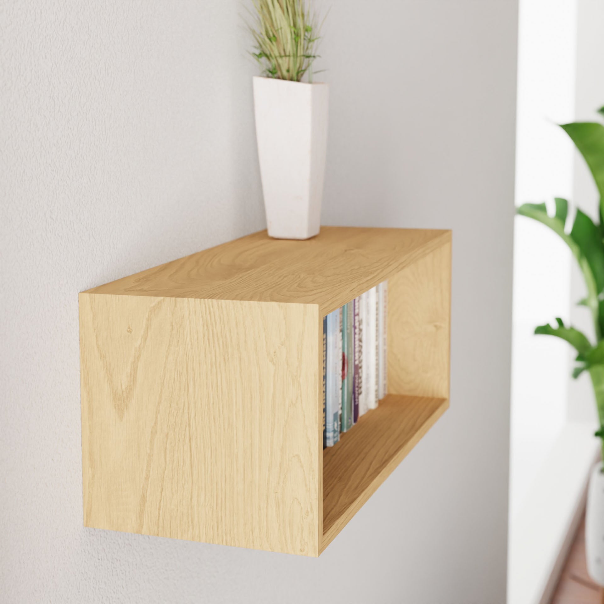 A Krovel "Floating Bookshelf in Maple" is mounted on a white wall, holding books and a white vase with vibrant green plants. A leafy plant adds nature to the background on the right.