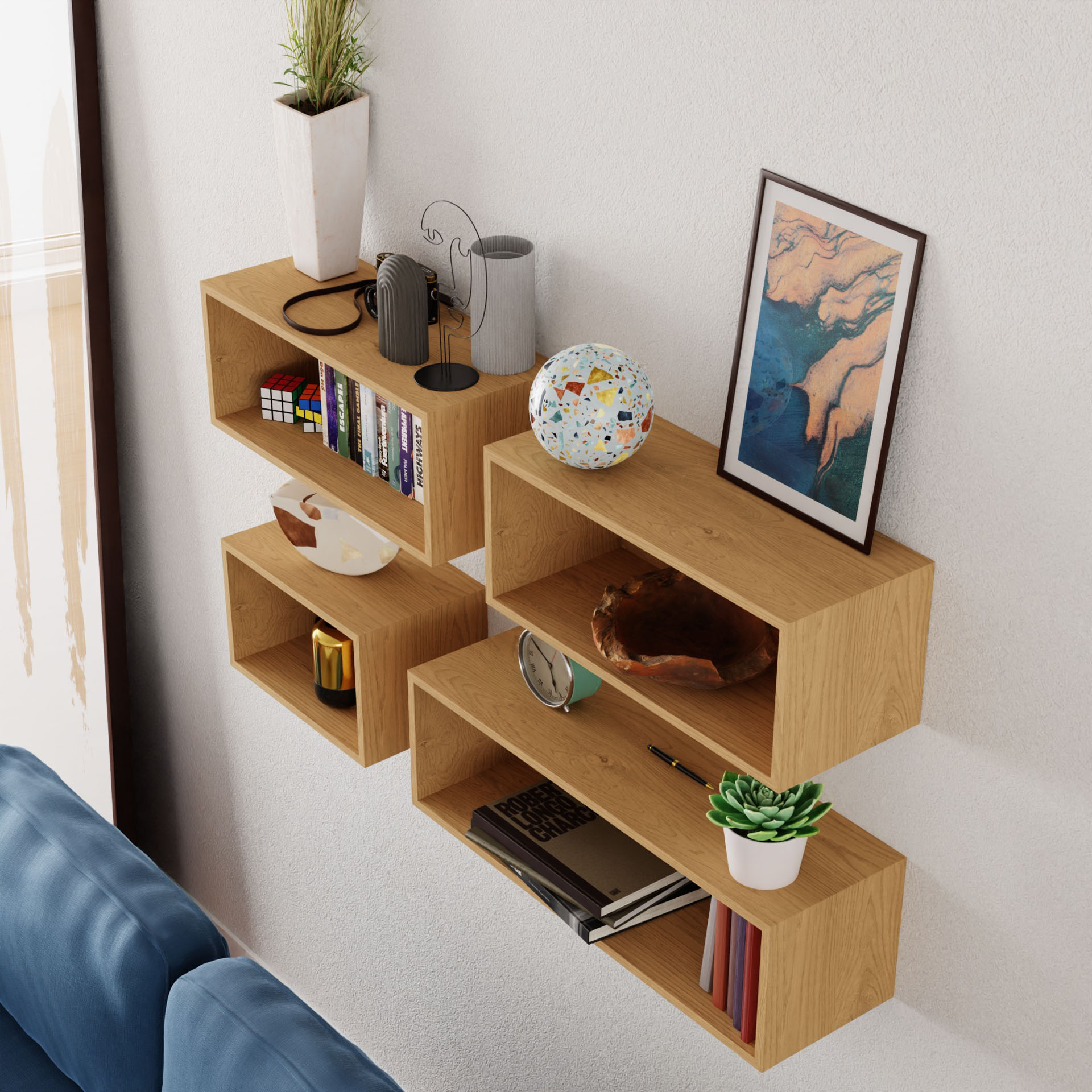 The Krovel Floating Bookshelf in Maple elegantly displays books, small plants, a decorative globe, and framed art. A blue sofa is partially visible below these wall-mounted shelves, which enhance the room's cozy and organized aesthetic.