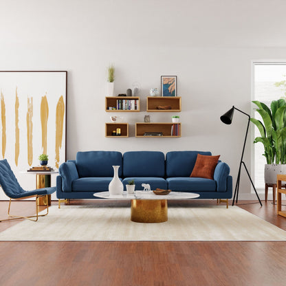 A modern living room showcases a blue sofa, a white coffee table, and a chic blue chair. Above the sofa are Krovel's Floating Bookshelf in Maple, displaying books and decor. On the left side, an abstract painting and black floor lamp add style to the room, while a plant on the right brings greenery to this American Hard Maple-accented space.