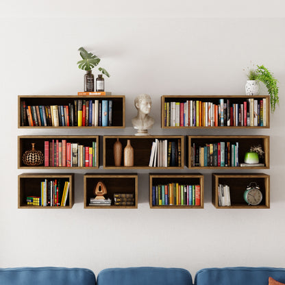 The Krovel Floating Bookshelf in White Oak is a modern, handmade, wall-mounted piece with staggered rectangular shelves. It holds books, a bust sculpture, vases, a globe, a plant, and an alarm clock while elegantly floating against a white wall above a blue sofa.