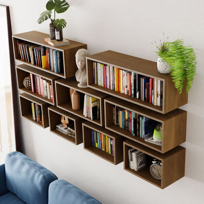 Krovel's Floating Bookshelf in White Oak elegantly showcases various books, a bust sculpture, and small decorative plants. The handmade wooden shelves are wall-mounted in a staggered pattern above a blue sofa.