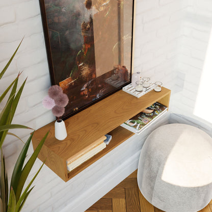 A cozy corner showcases a wooden shelf filled with books, magazines, and glasses. Atop the Krovel Floating Console Table in Cherry, a white vase displays a fluffy decorative item in perfect harmony with the mid-century modern aesthetic. A large framed painting is elegantly hung above. Nearby, a round cushioned stool sits on the American Cherry floor while a plant adds vibrant greenery to the scene.