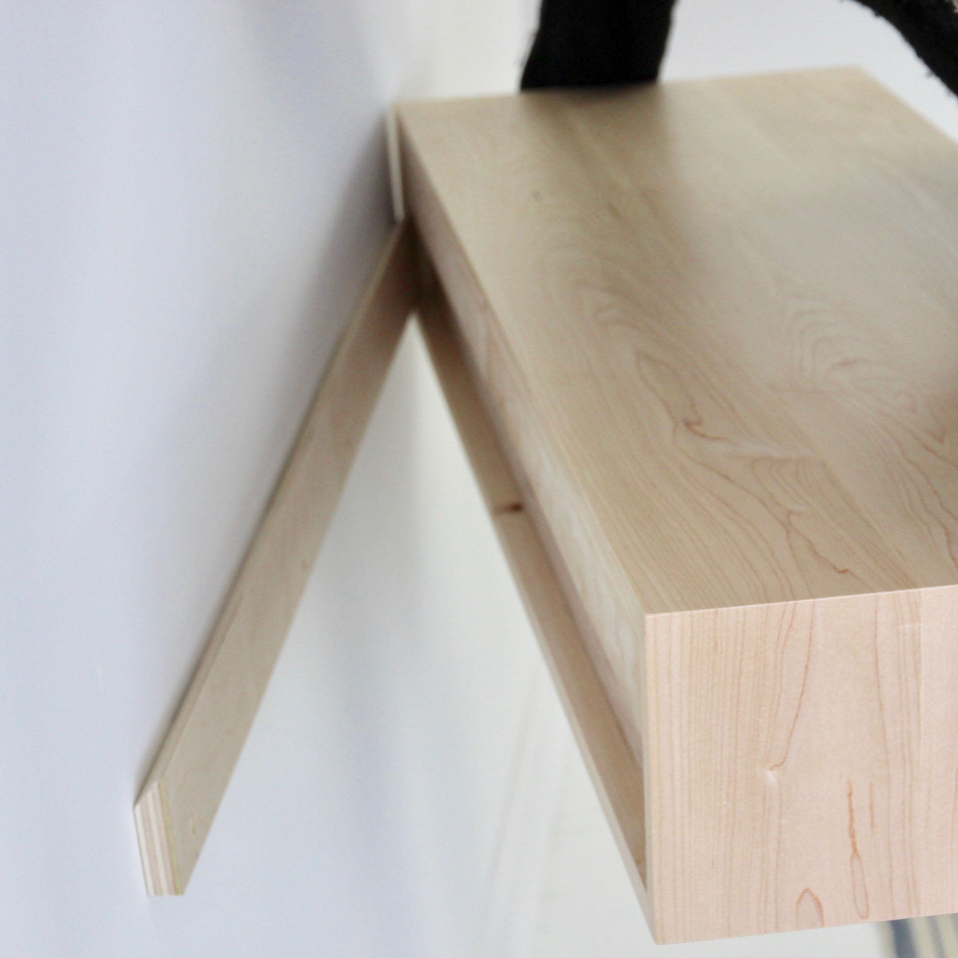 A Floating Desk in Maple by Krovel is being installed against a white wall, showcasing its light wood finish. A black support bracket is visible beneath it. The sleek, modern design, enhanced with VOC-Free Polymerized Linseed Oil, shines in the simple, minimalist setting.
