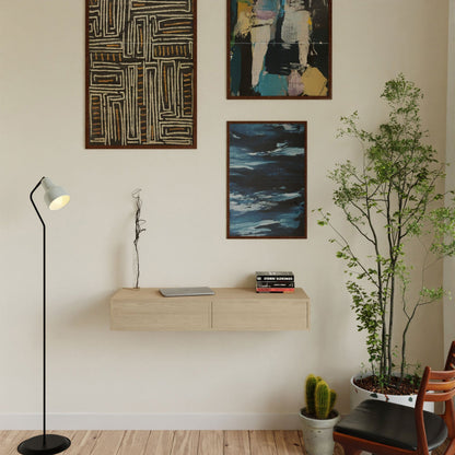 A minimalist interior showcases three abstract paintings on a light-colored wall. A floating desk in Maple by Krovel complements a wooden shelf displaying books and a sculpture. Nearby, a tall potted plant and cactus highlight the modern floor lamp and two wooden chairs, crafted with VOC-free polymerized linseed oil.