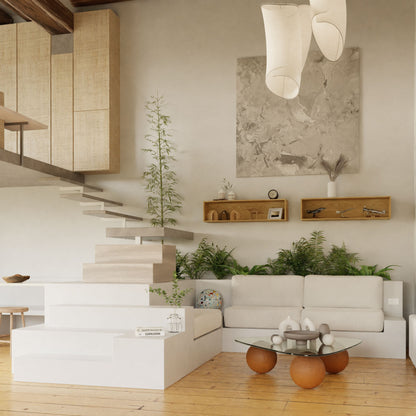 A modern living room with solid oak flooring, a white sectional sofa, and a staircase with open wooden steps. Green plants adorn the space. Two Krovel Floating Display Cases in White Oak and a large abstract painting decorate the wall. A glass coffee table with round stools is nearby.