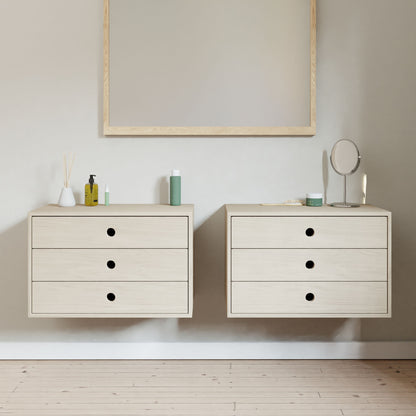 The minimalist bathroom features two Krovel Floating Dressers in Maple with soft-close slides, three drawers each, and black knobs. A large rectangular mirror with a light wood frame hangs above. Light wooden flooring seamlessly complements the neutral decor.